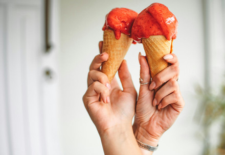 Two intertwined hands holding two cones of icecreams